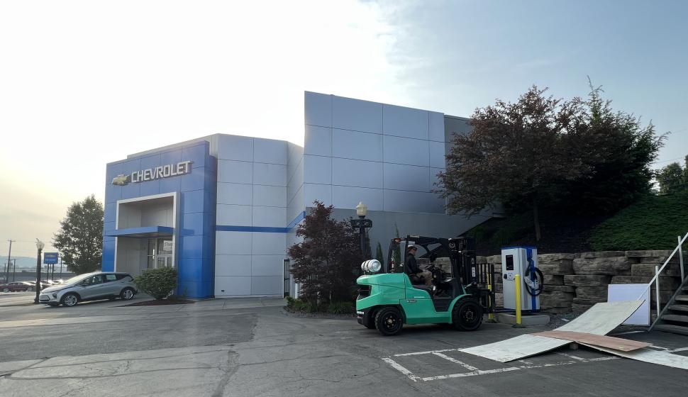 Wide shot of electrician on forklift setting exterior commercial Level 3 DC Fast Charging EV charger outside of Chevrolet dealership