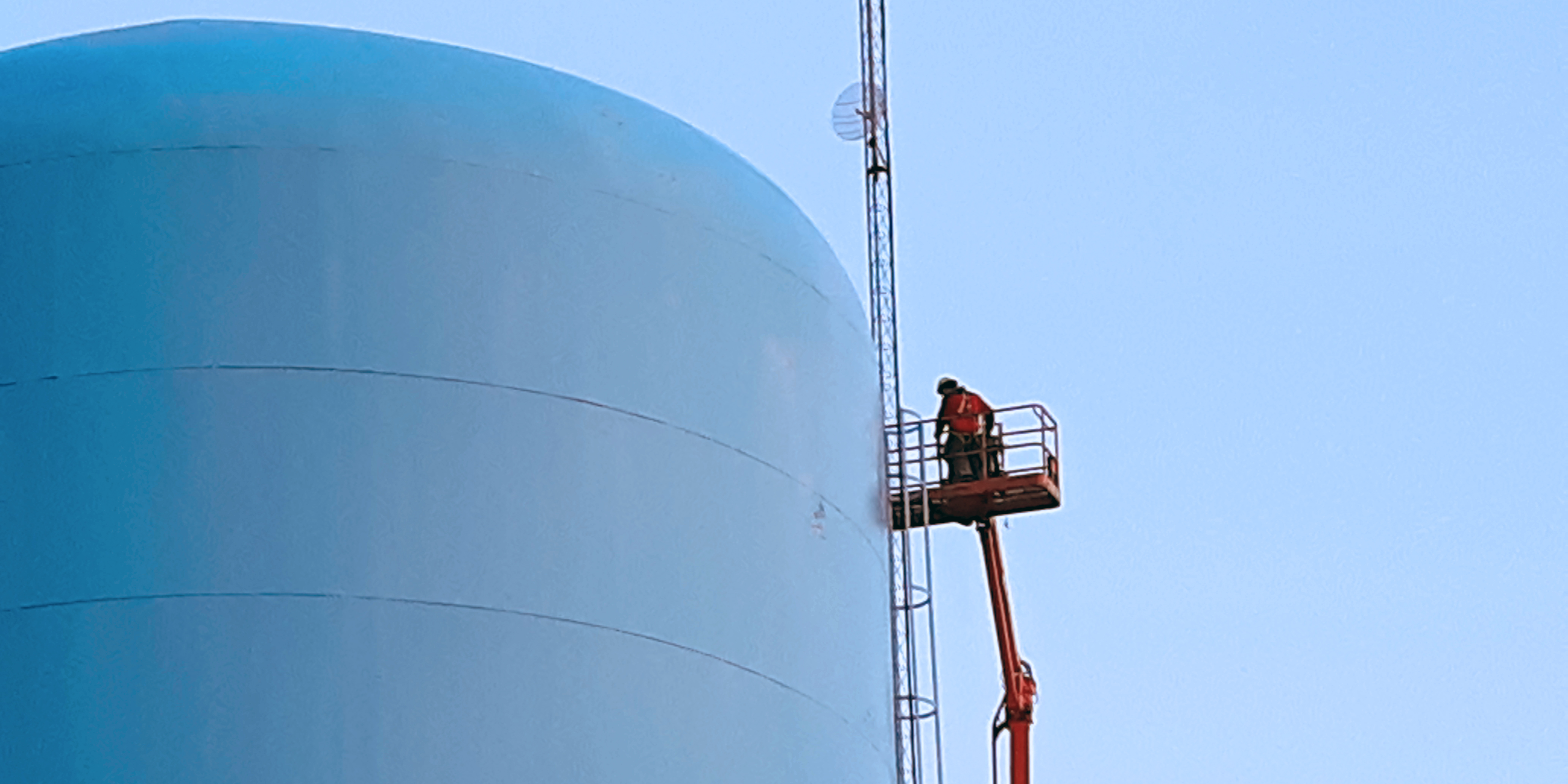 Technician on fully extended man lift servicing electrical components at the top of a water tower