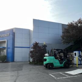 Wide shot of electrician on forklift setting exterior commercial Level 3 DC Fast Charging EV charger outside of Chevrolet dealership