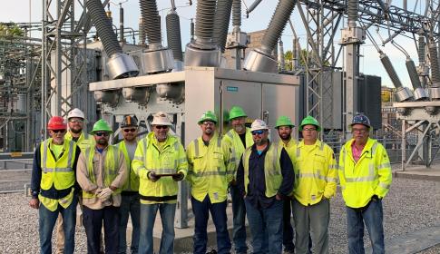 Linemen pose with award in front of substation transformers