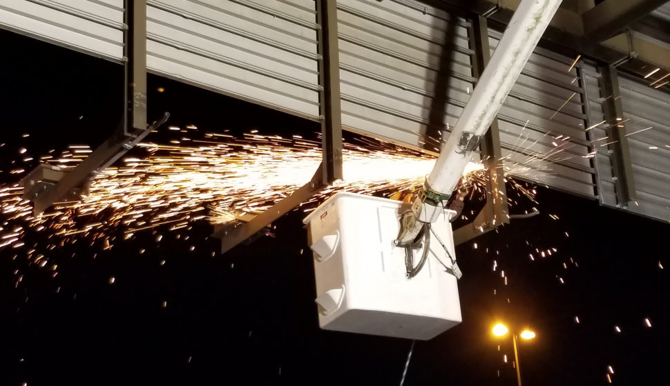 Sparks fly from an overhead highway sign structure