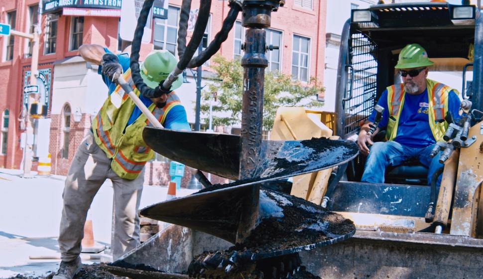 Construction drilling with man and shovel and man in skid steer