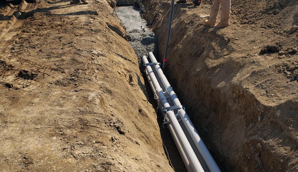 Construction team pouring concrete over fiber-optic duct bank in trench