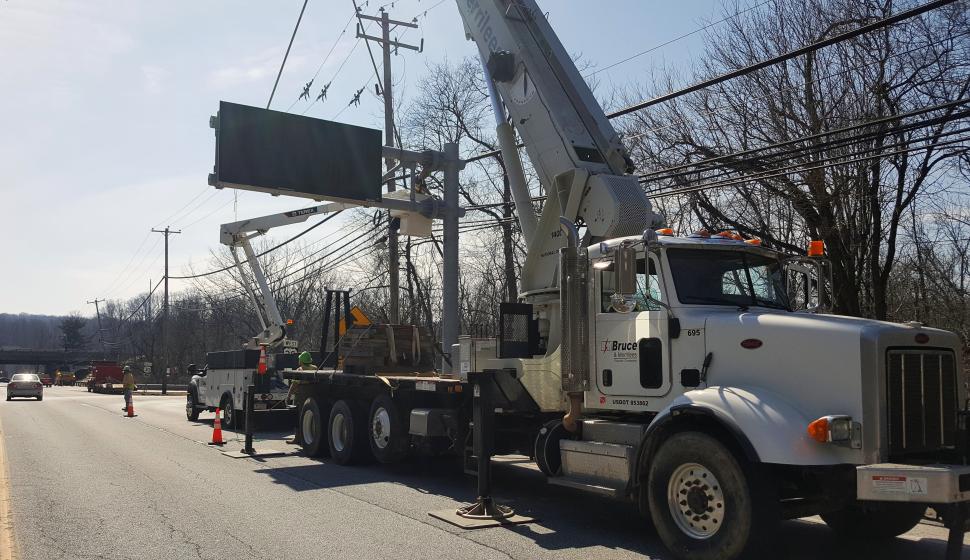 Highway construction crane setting Dynamic Message Sign (DMS) onto crossarm