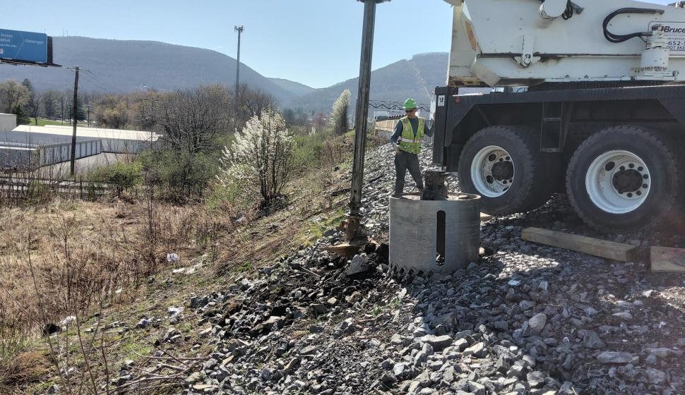 Heavy highway lighting foundation drilling with worker supervising