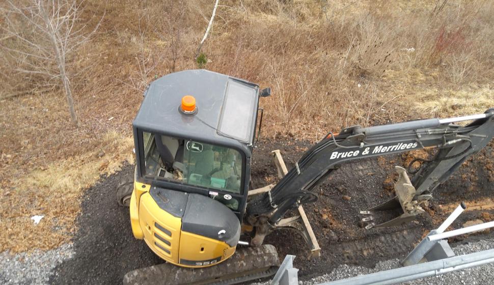 Mini excavator moving earth along side of highway