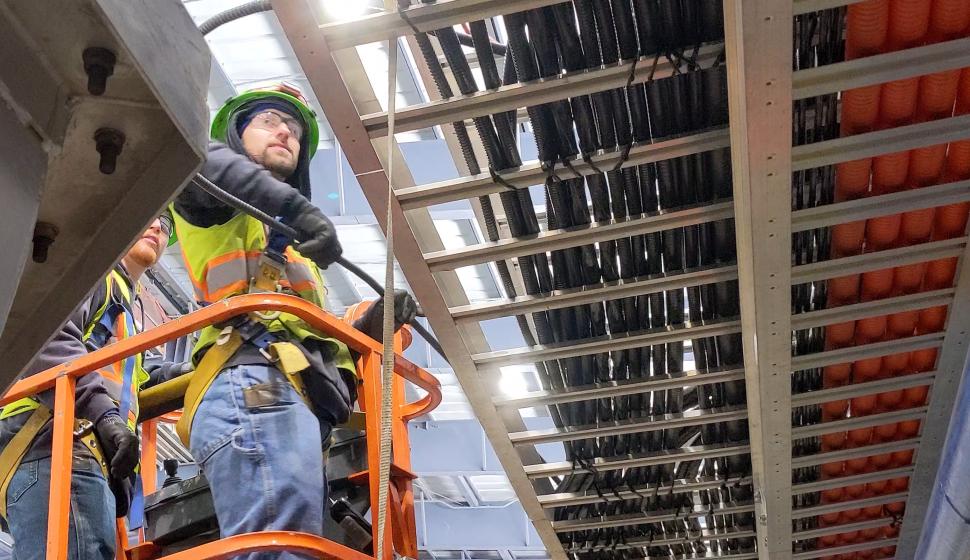 Electricians on lift pull cable for walking beam furnace; cable tray in foreground