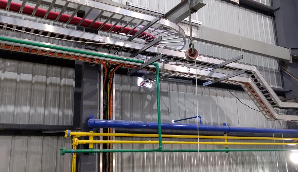 multiple cable trays with multi-colored pipe fittings on interior wall of walking beam furnace building